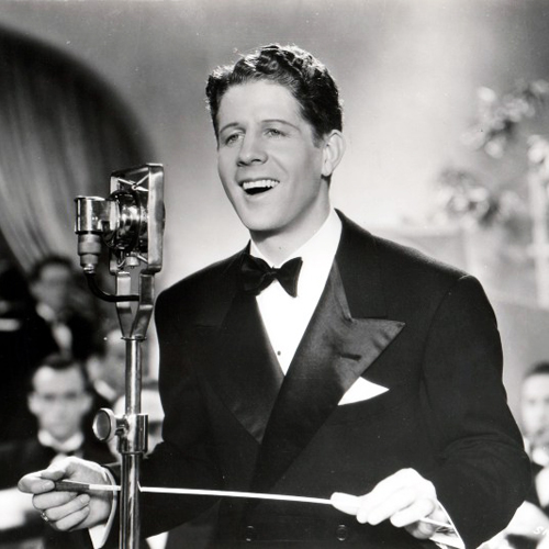 Singer Rudy Vallée holding a conductor's baton whilst singing into microphone